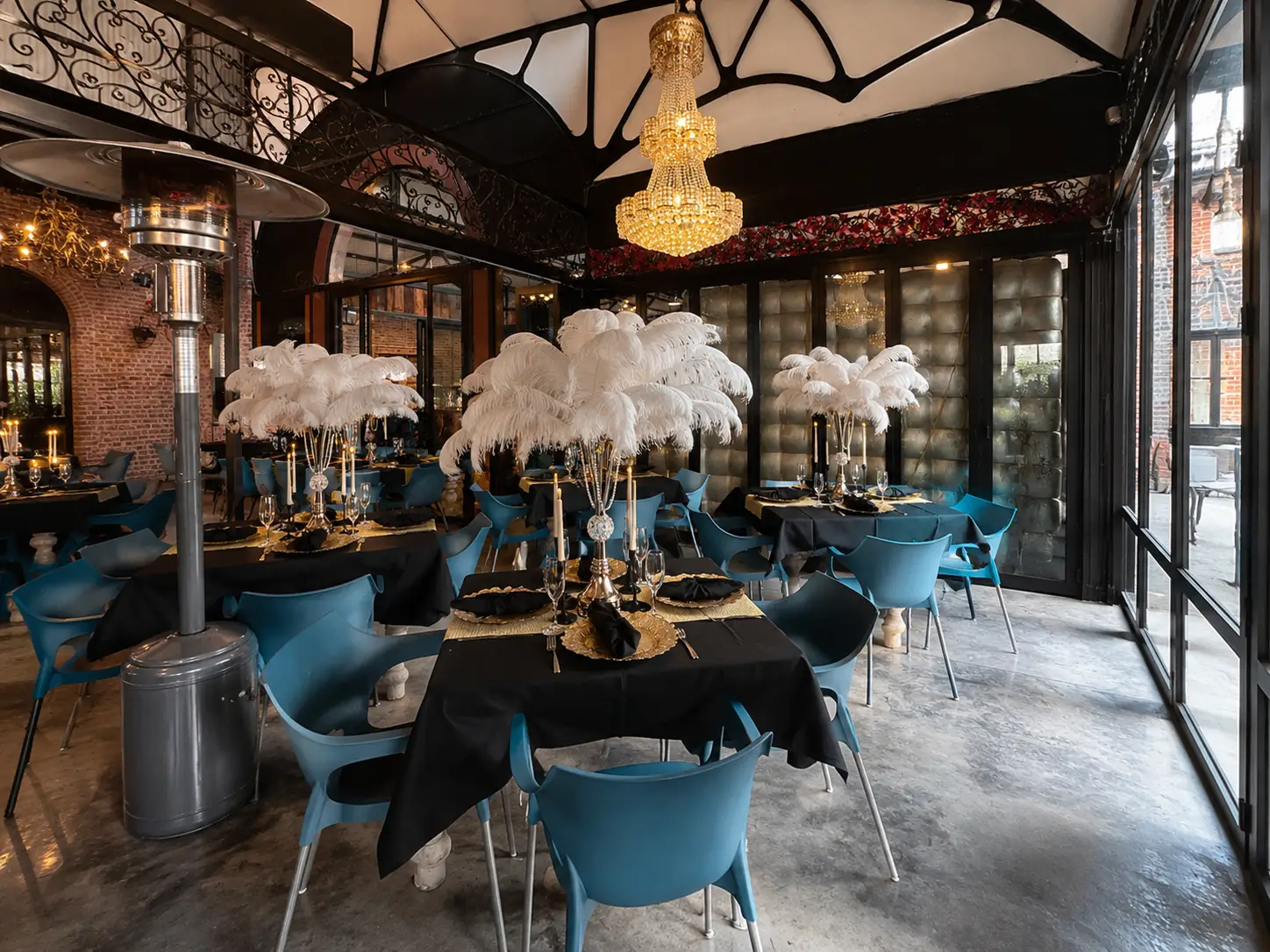 Elegant dining room with black-tablecloth tables, blue chairs, white feather centerpieces, and chandelier.