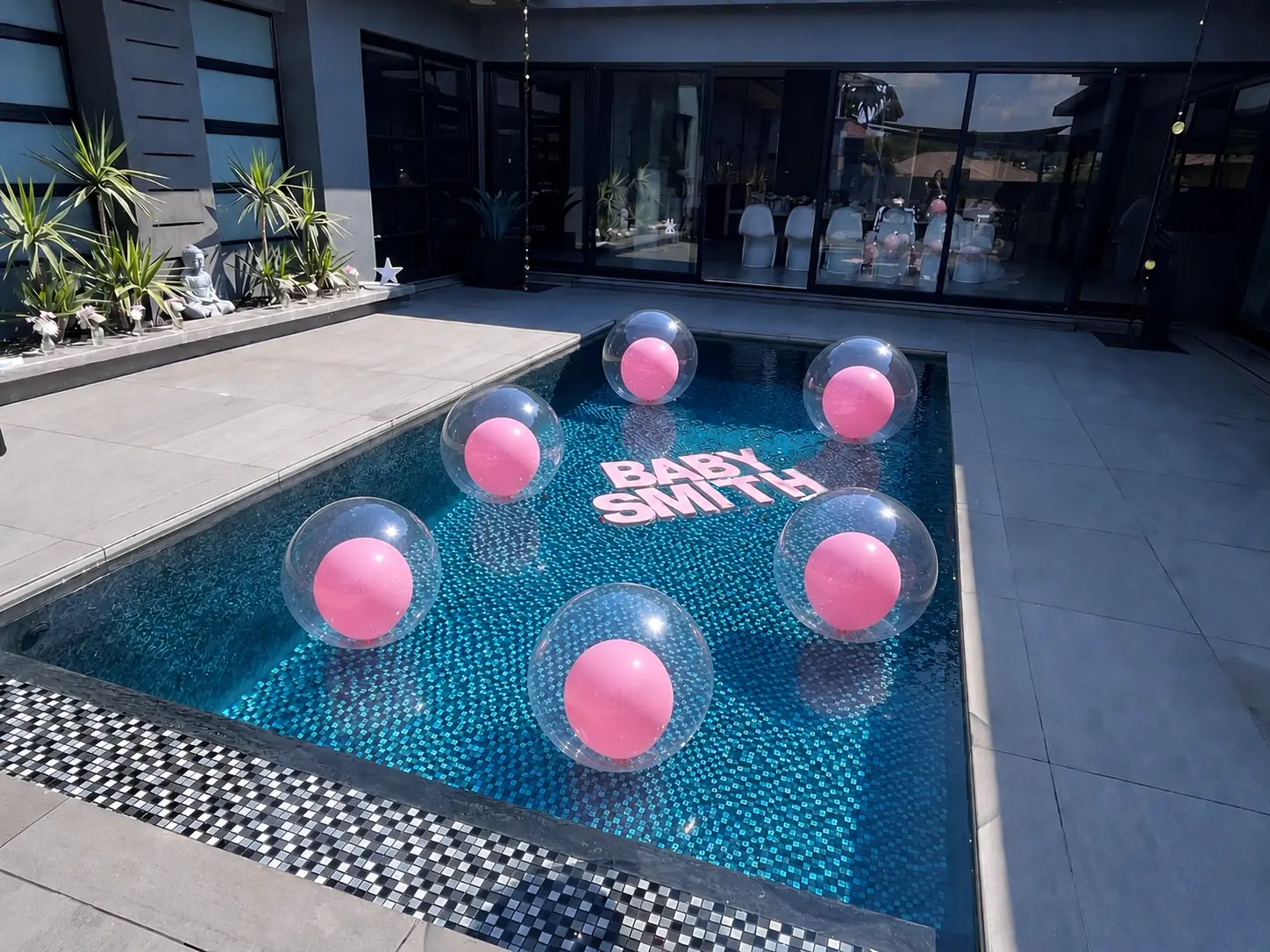 Pool with pink balloons inside clear balloons floating around pink letters spelling BABY SMITH.
