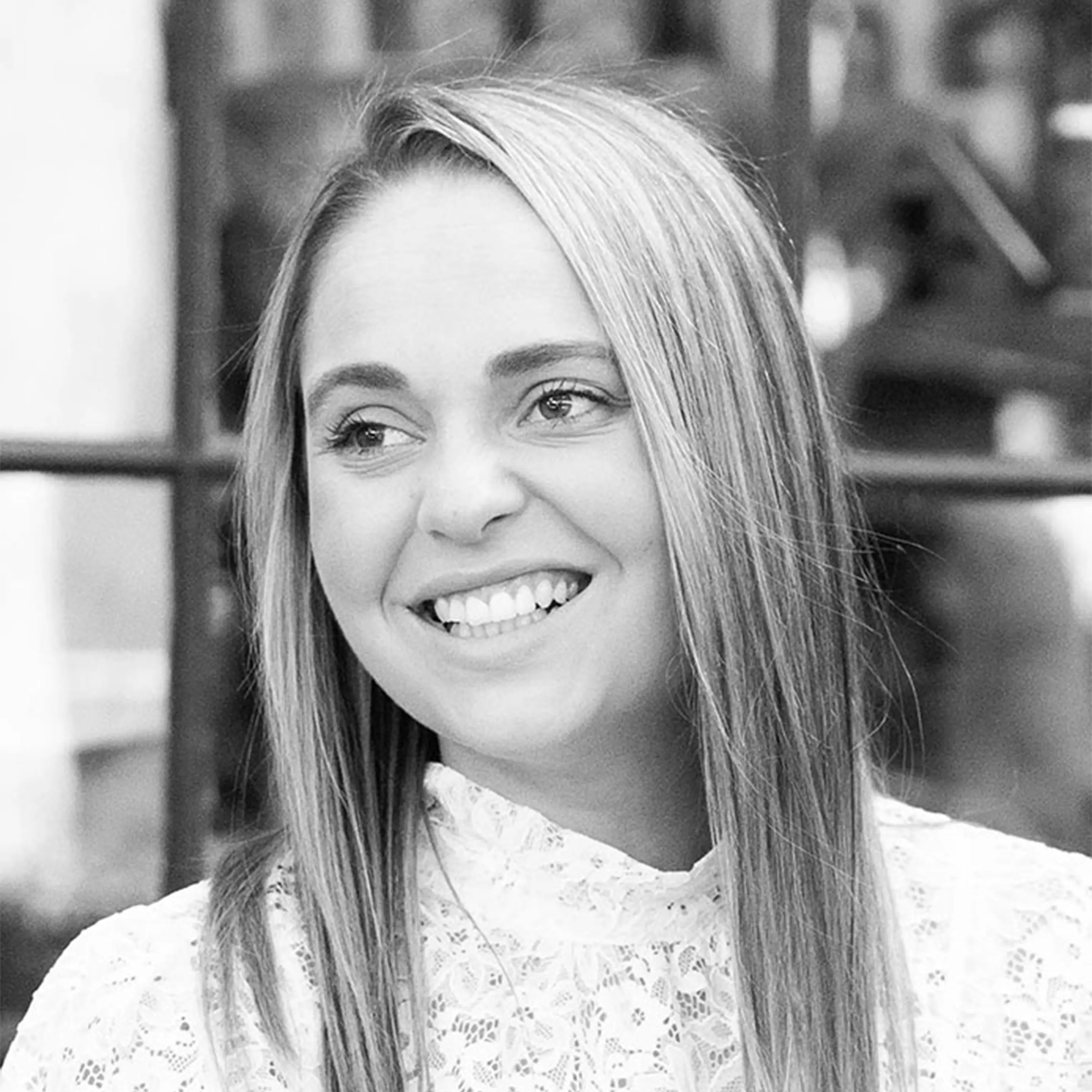 Smiling woman with long straight hair wearing a white lace top looking to her left.