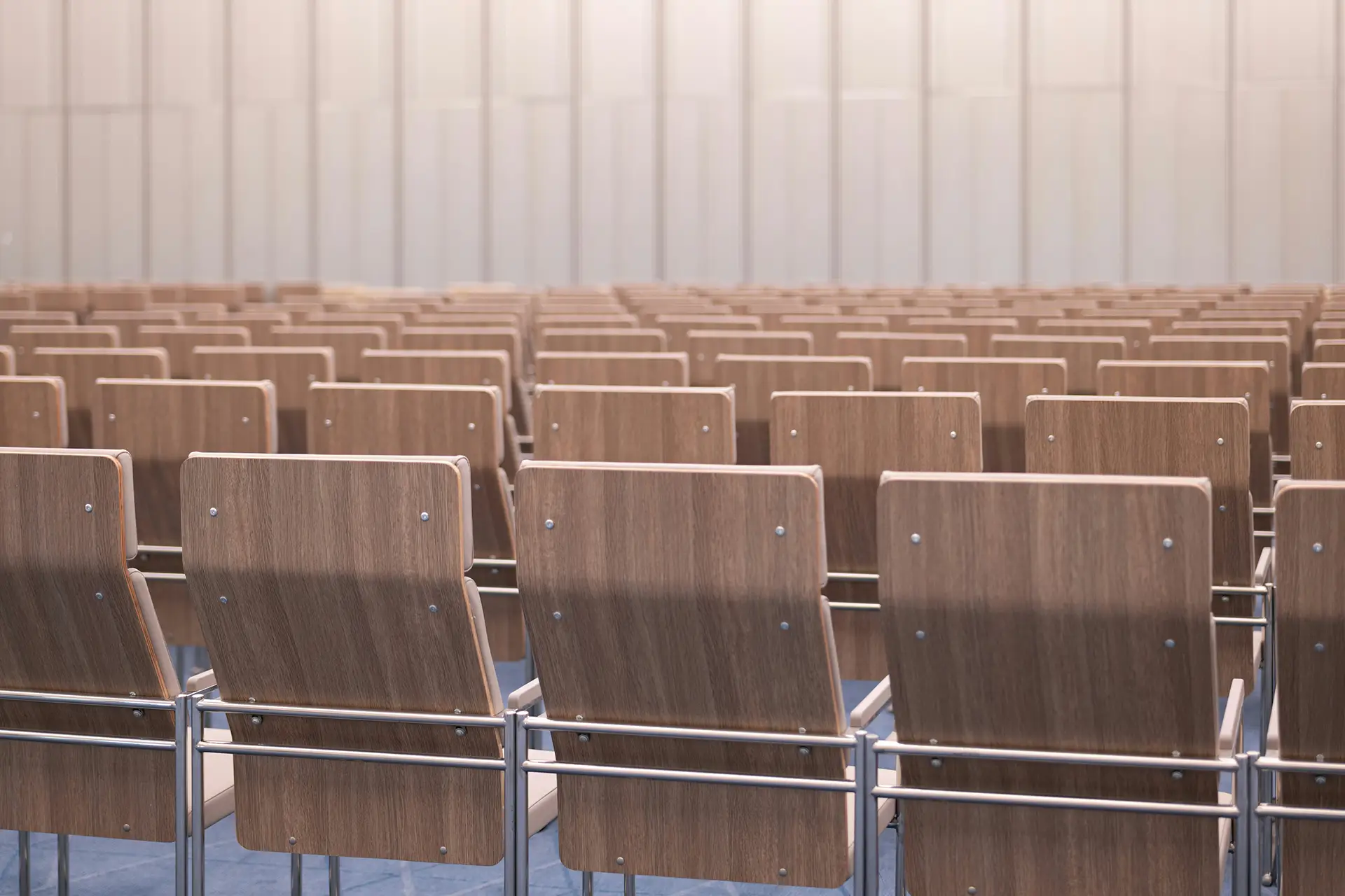Rows of empty wooden chairs with metal frames in a large conference room or auditorium.