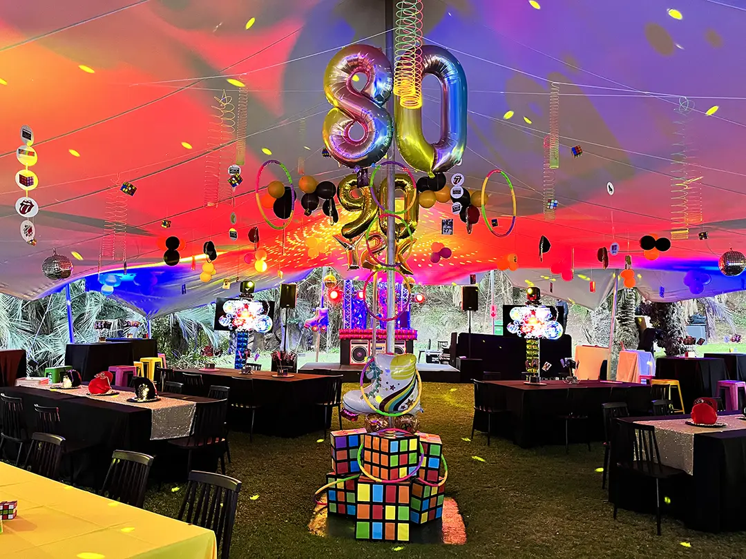 Colorful 1980s themed party tent with balloon numbers 80, disco balls, Rubik's cubes, and neon lights.