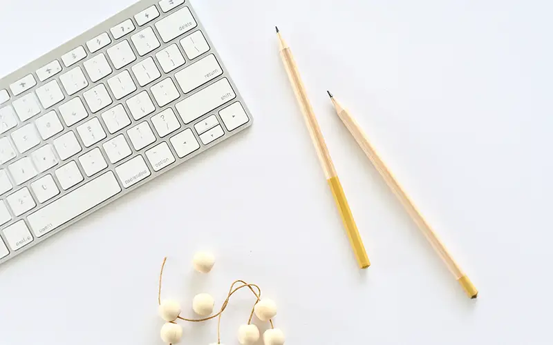 White computer keyboard, two yellow-tipped pencils, and a string of wooden beads on a white surface.