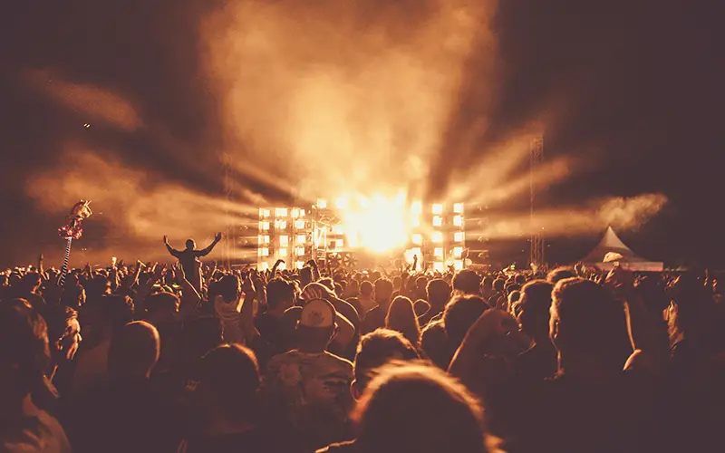 Crowd enjoying nighttime concert with bright stage lights and smoke effects.