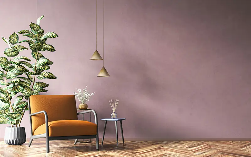 Orange armchair beside a potted plant, small table with decor, and two hanging pendant lights on a wooden floor.
