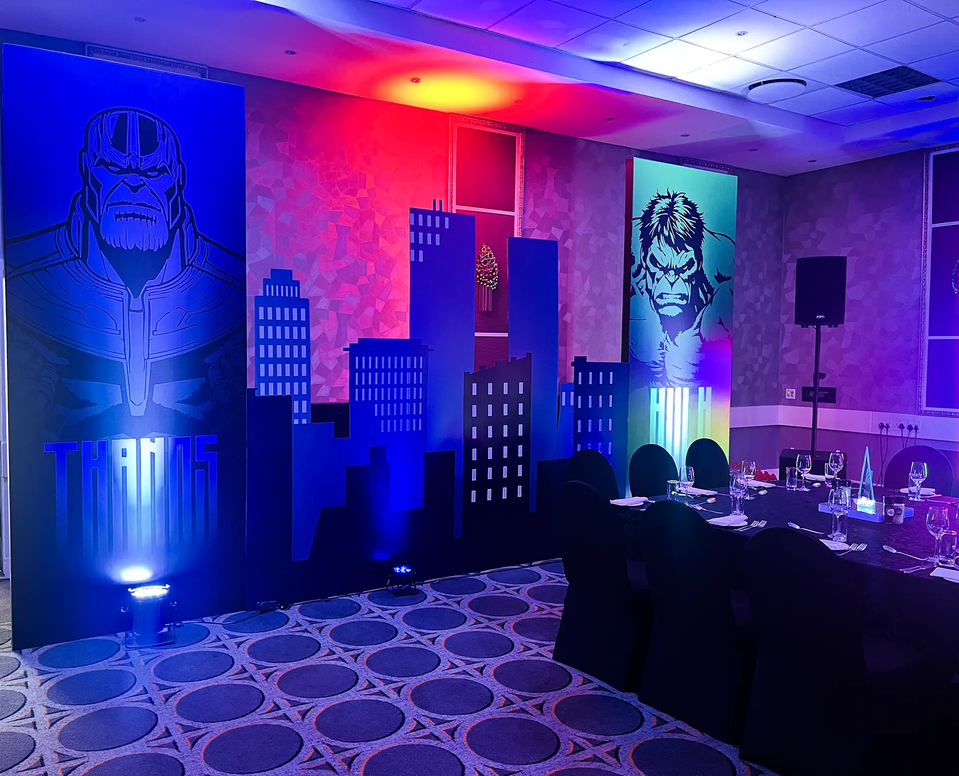 Event room with Marvel Thanos and Hulk posters, city skyline backdrop, and a table set for dining.