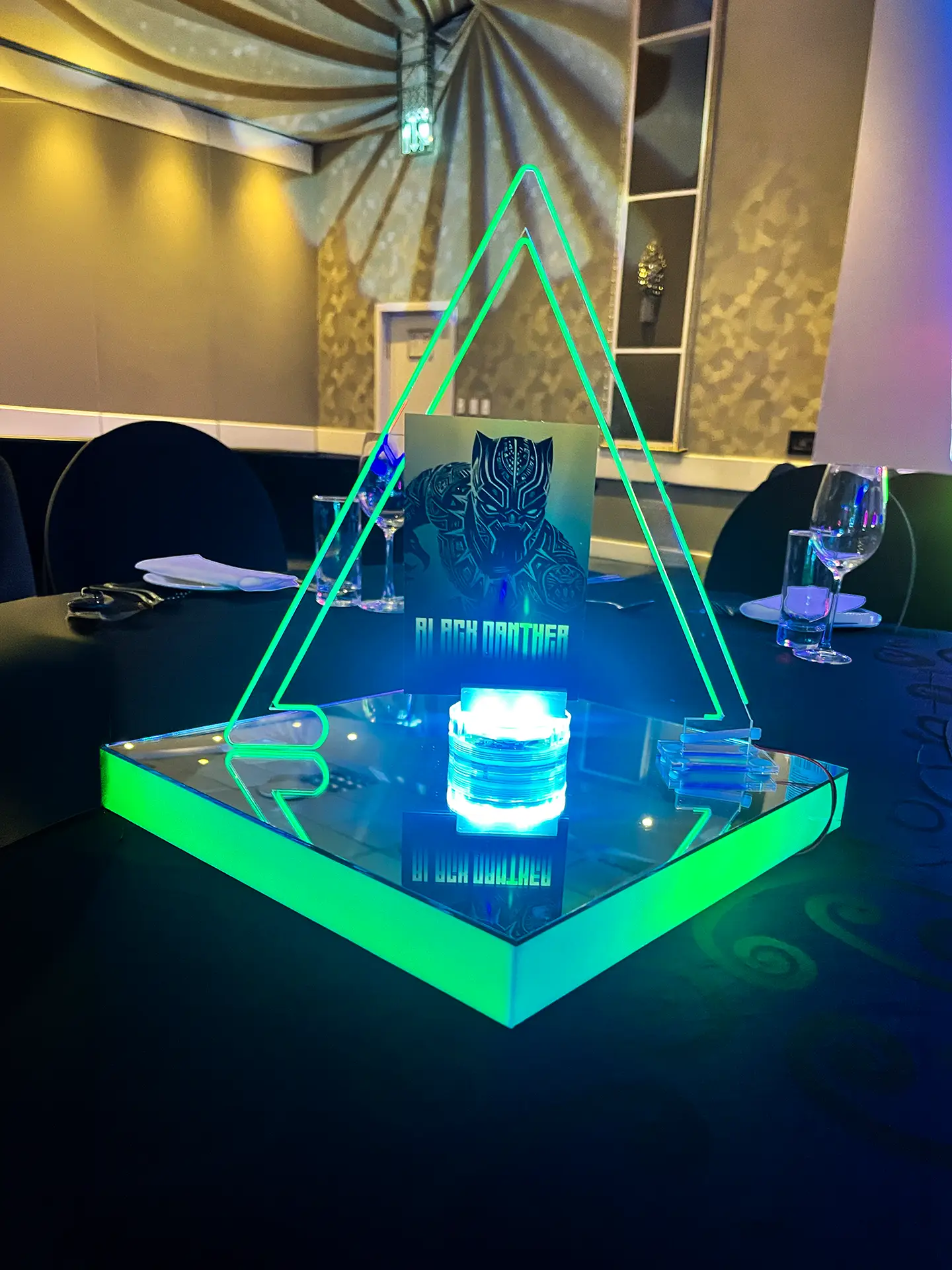 Table centerpiece with glowing green triangle frame and Black Panther image at a dimly lit event.