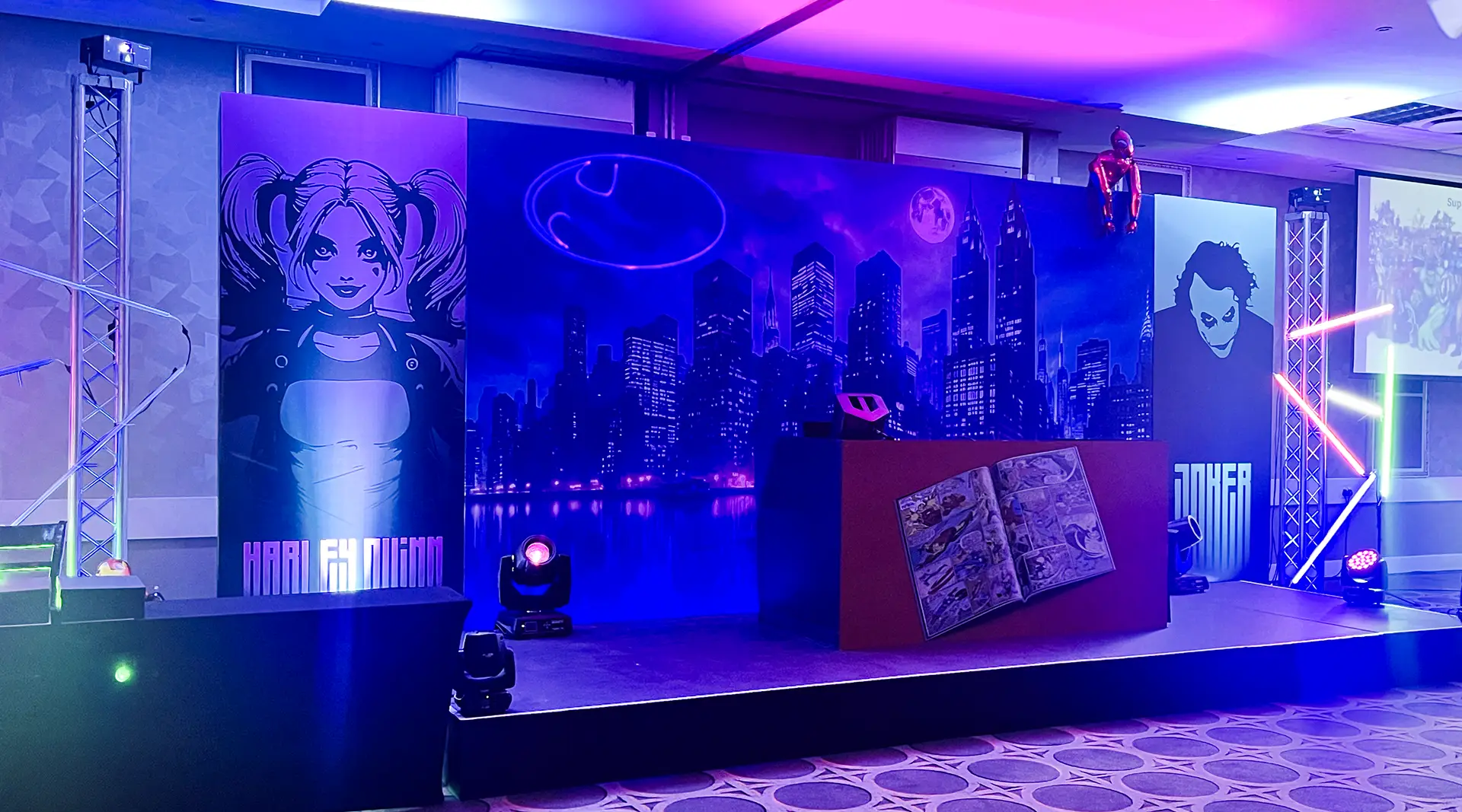 Stage with neon lights, comic book cityscape backdrop, and portraits of Harley Quinn and Joker characters.