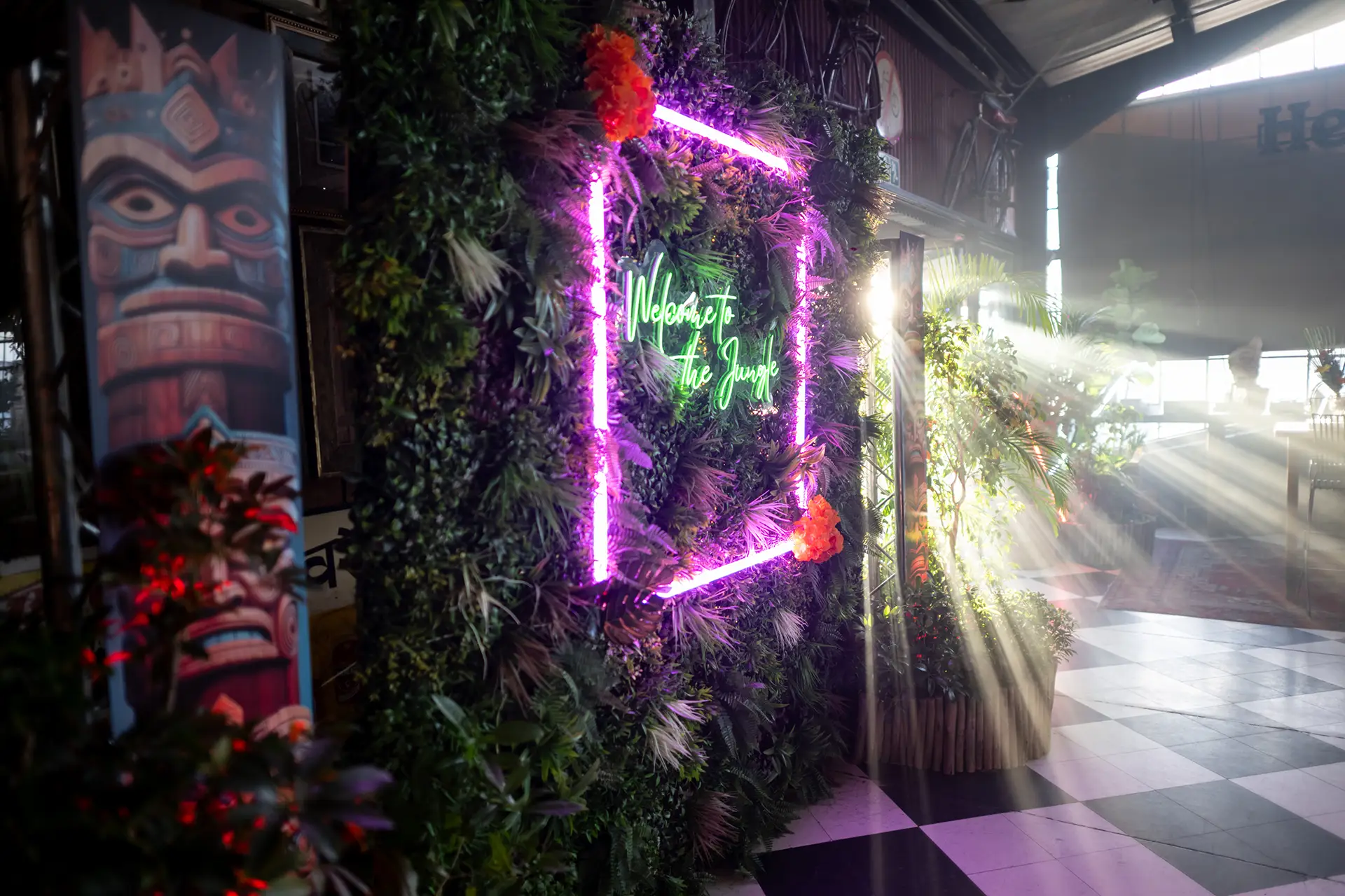 Indoor jungle-themed wall with neon sign reading Welcome to the Jungle and sunlight streaming in.