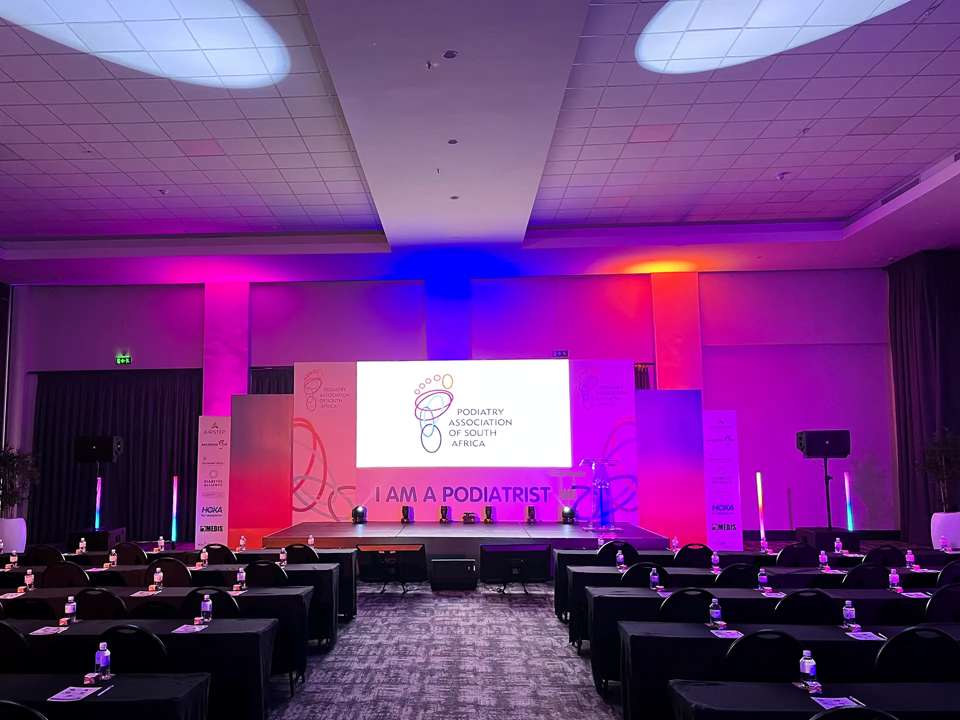 Conference room with stage and screen showing Podiatry Association of South Africa logo.