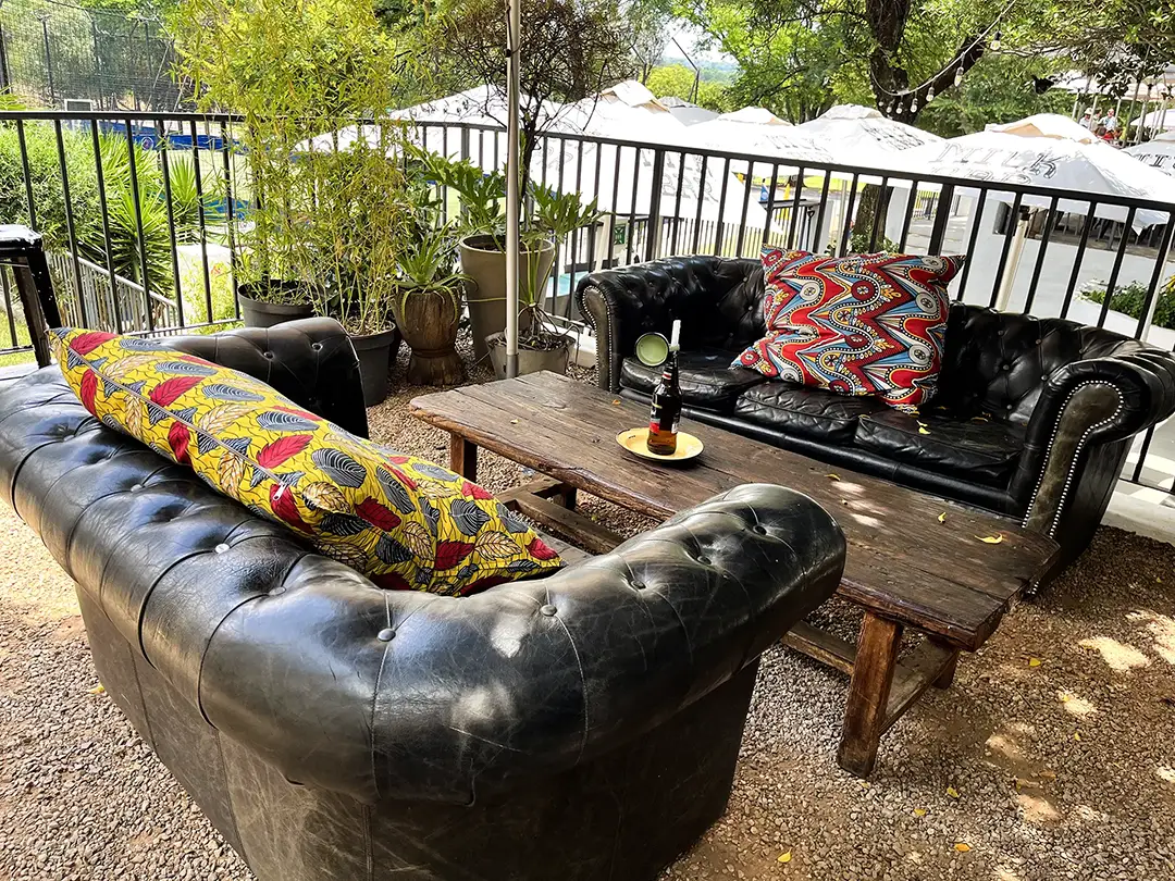 Outdoor seating with two black leather sofas, colorful pillows, and a wooden table with a bottle and cup.
