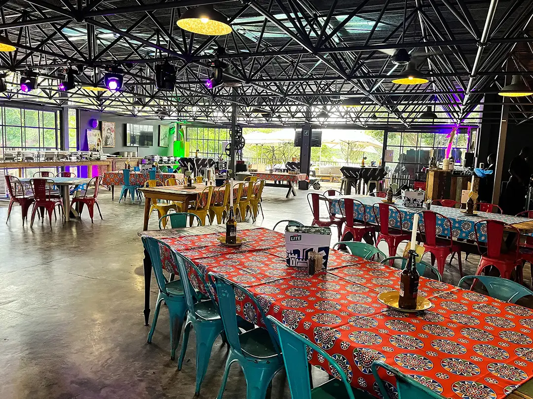 Spacious colorful restaurant interior with patterned tablecloths and metal chairs under exposed beams.