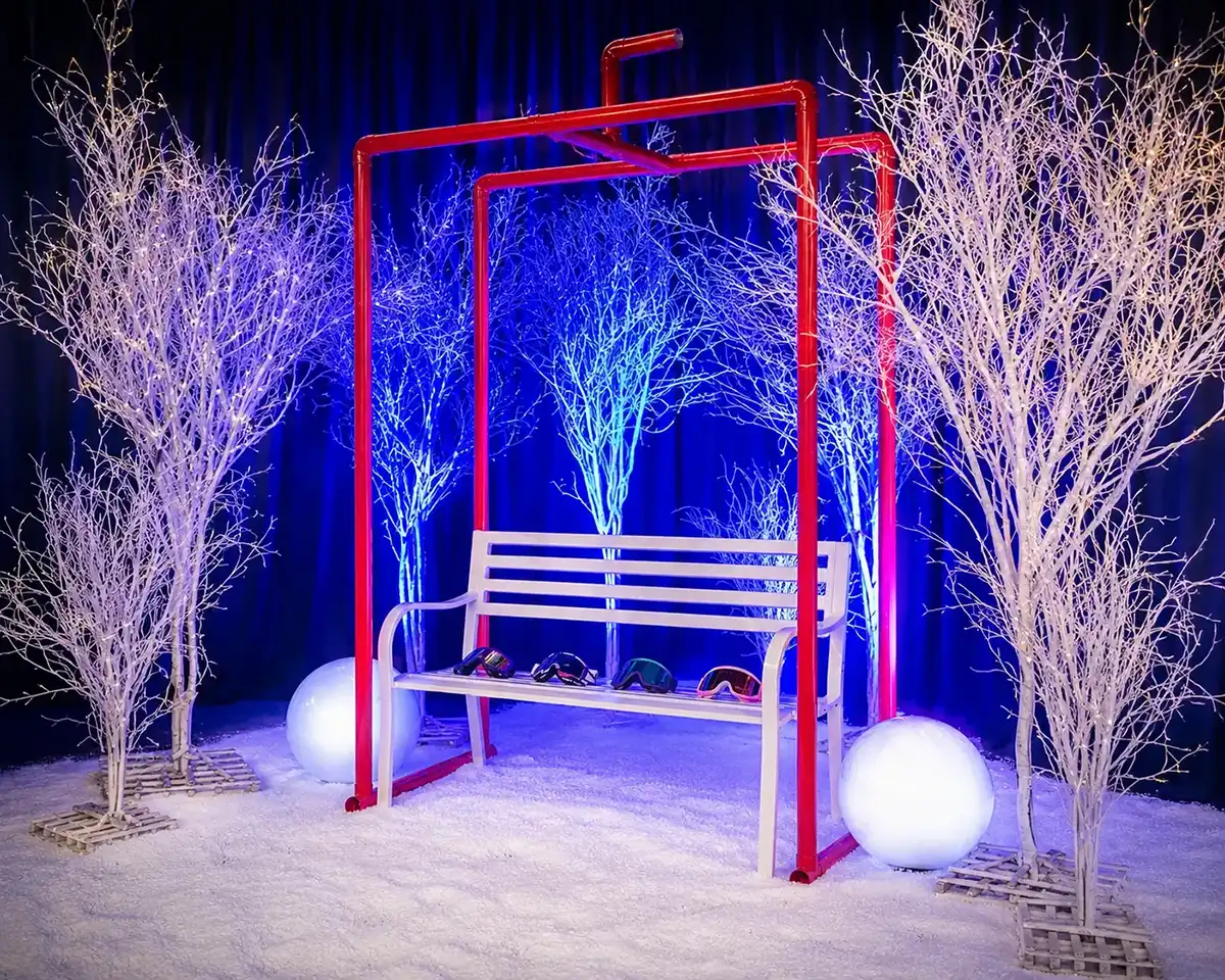 A display which is a ski lift with a white bench, ski goggles on the bench and a bench frame for the lift