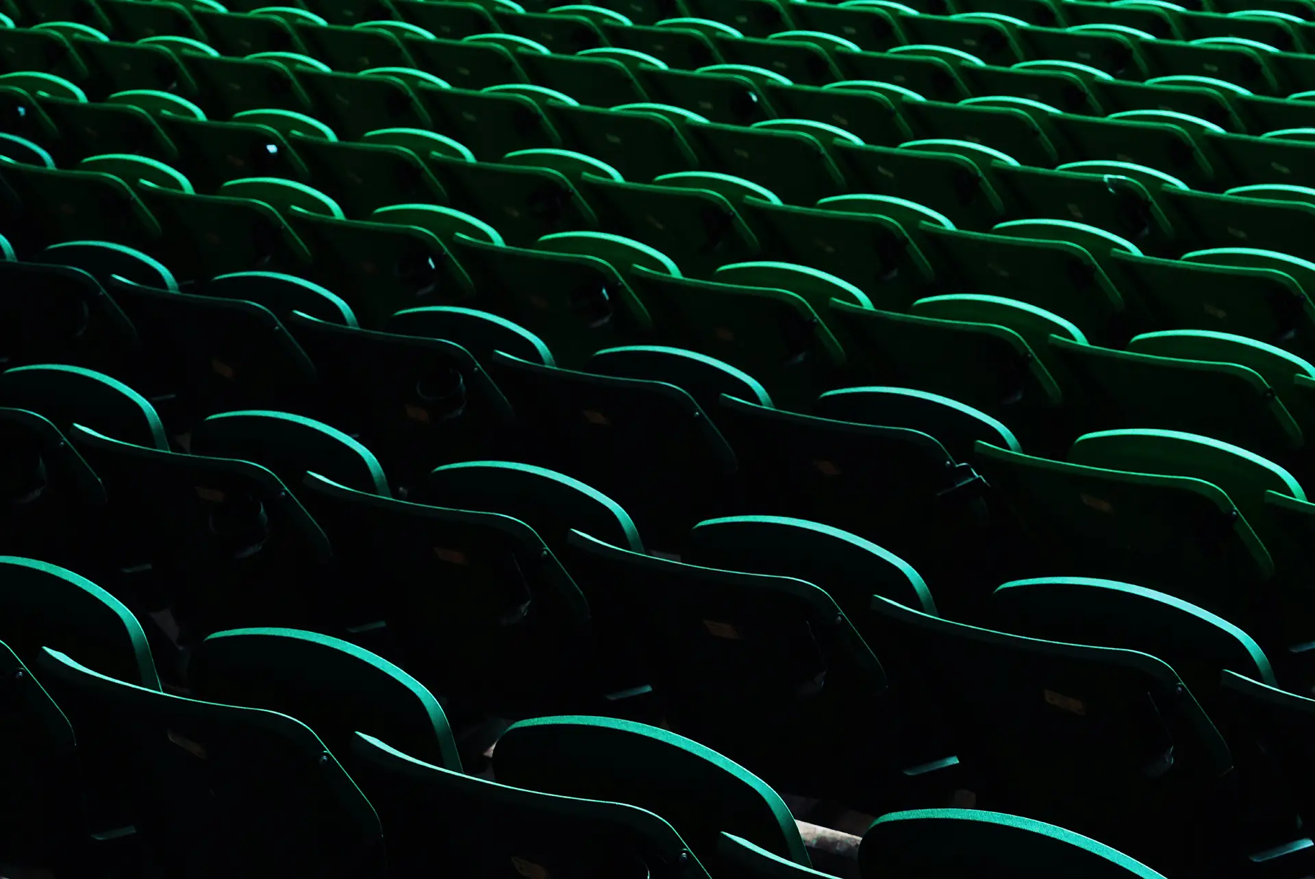 Row upon row of empty green stadium seats captured in low light creating a pattern of curves and shadows.