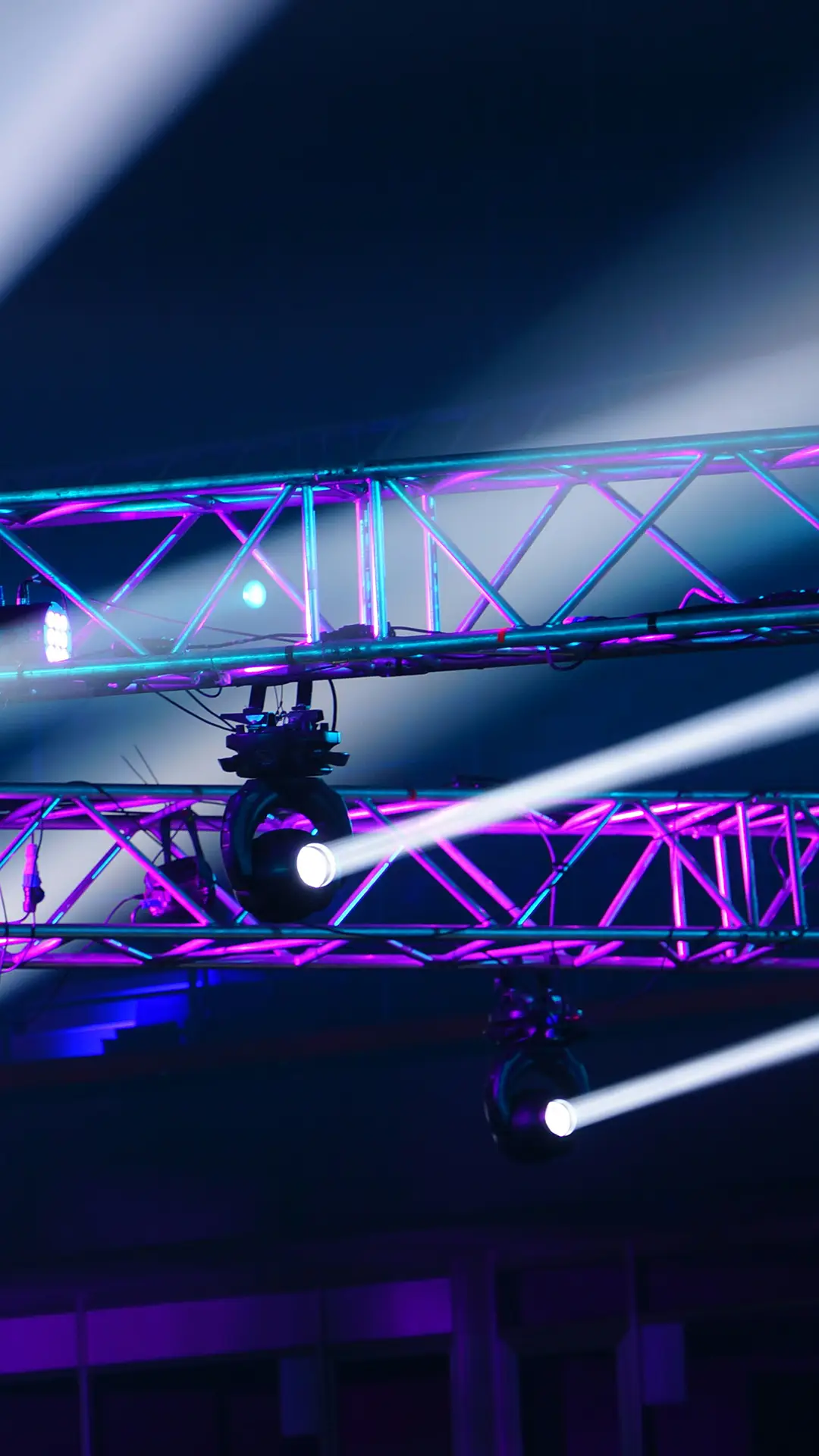 Stage lighting with purple-lit metal trusses and two spotlights beaming white light.